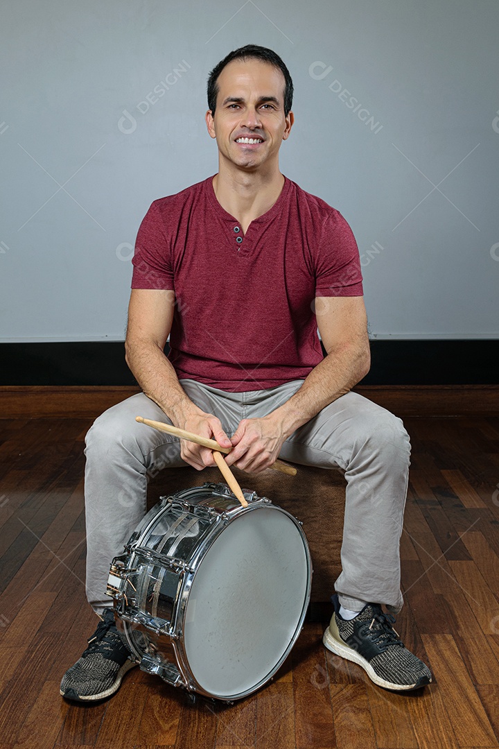 Homem de 44 anos sorrindo com caixa de bateria e baquetas