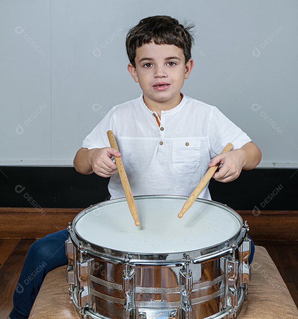 Criança de 7 anos olhando para a câmera e tocando bateria.