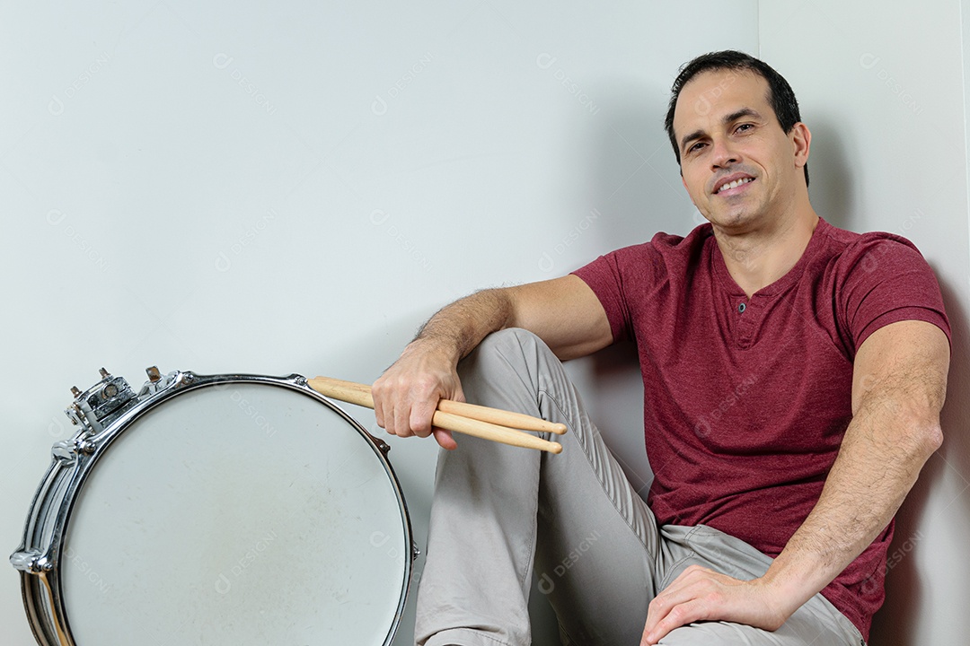 Homem de 44 anos sorrindo com caixa de bateria e baquetas