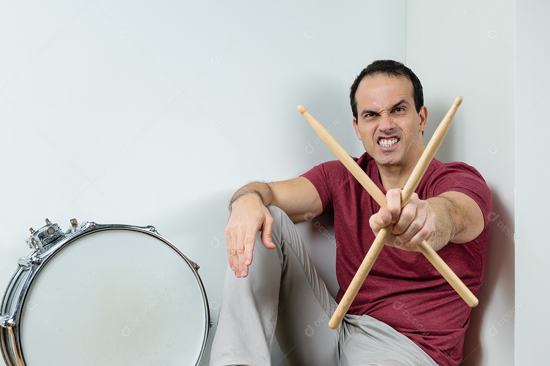 Homem de 44 anos sorrindo com caixa de bateria e baquetas