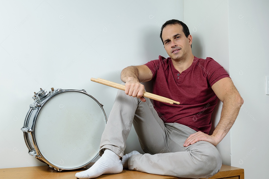 Homem de 44 anos sorrindo com caixa de bateria e baquetas