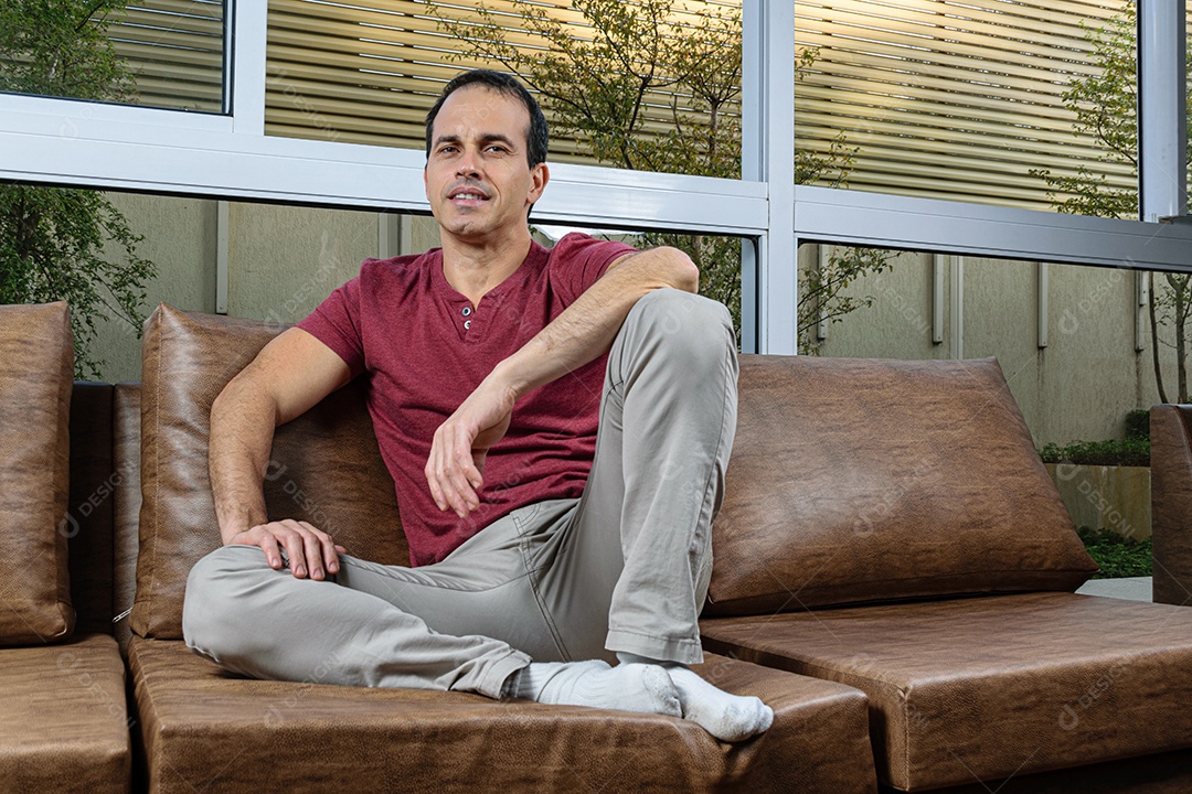 Homem jovem sentado sobre sofá sobre conforto de sua casa