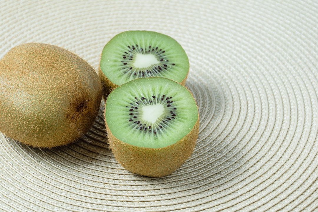Kiwi cortado ao meio sobre um tapete de palha de forma circular.