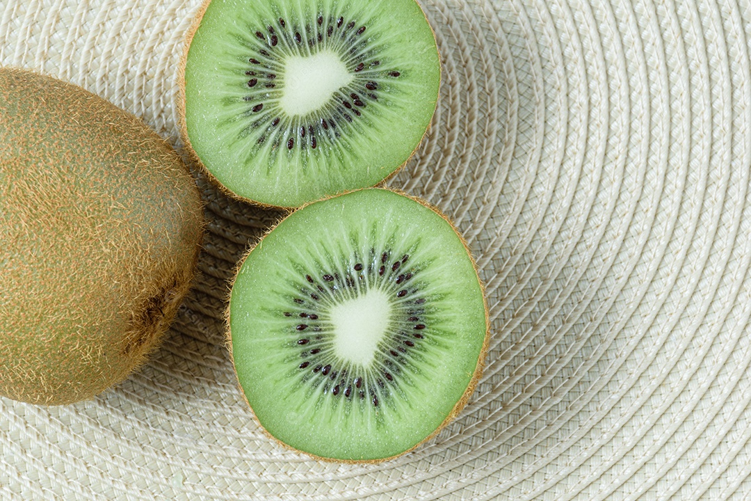 Kiwi cortado ao meio sobre um tapete de palha de forma circular.