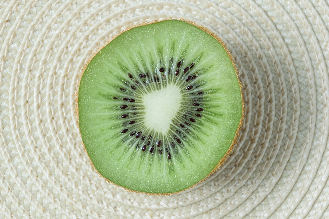 Kiwi cortado ao meio sobre um tapete de palha de forma circular.