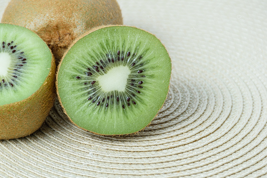 Kiwi cortado ao meio sobre um tapete de palha de forma circular.