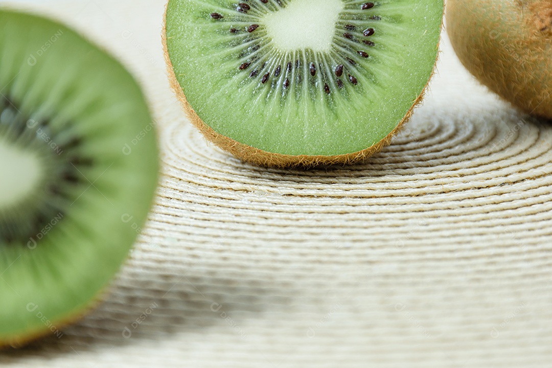 Kiwi cortado ao meio sobre um tapete de palha de forma circular.