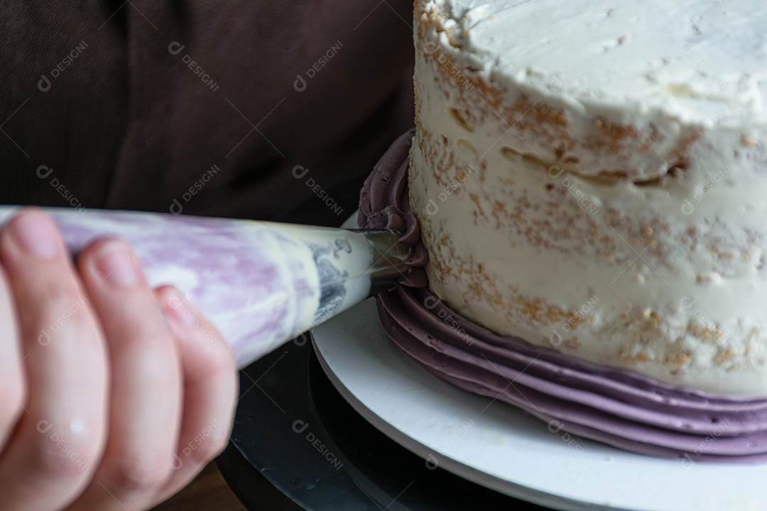 Confeiteiro usando o bico de confeiteiro para decorar o bolo de creme de manteiga roxo.