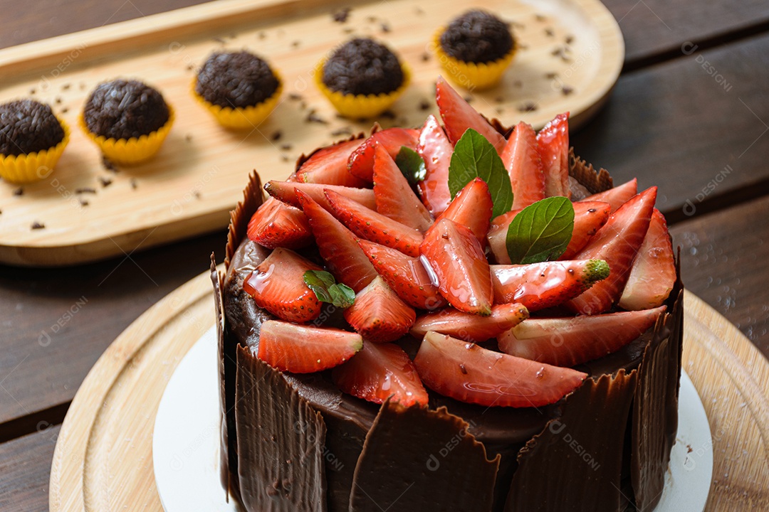 Bolo de chocolate sendo decorado coberto com morangos, folhas frescas de manjericão