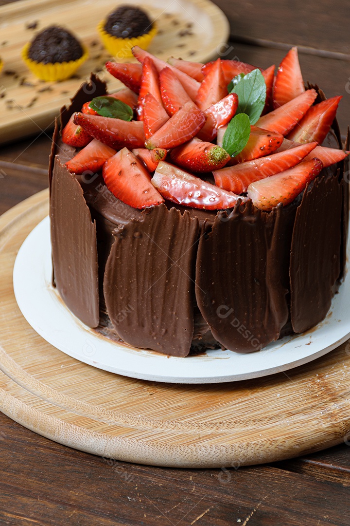 Bolo de chocolate sendo decorado coberto com morangos, folhas frescas de manjericão