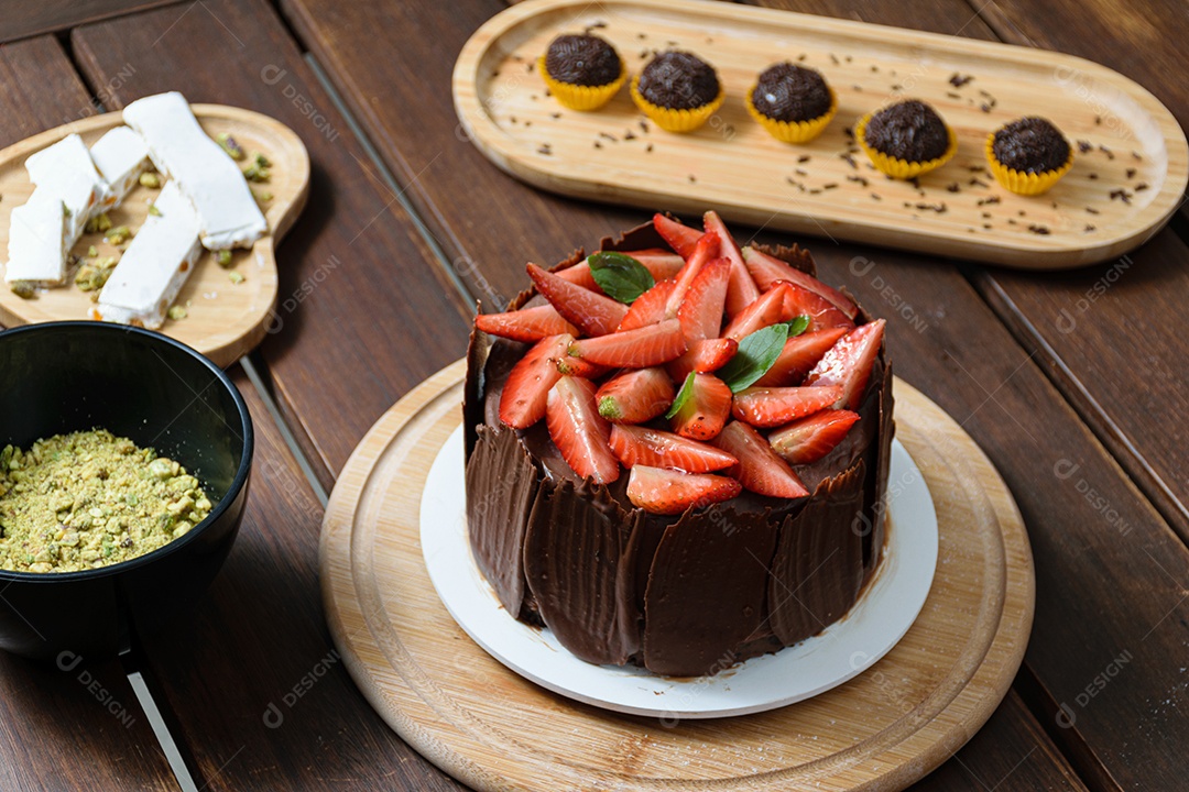 Bolo de chocolate sendo decorado coberto com morangos, folhas frescas de manjericão
