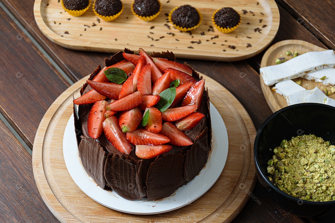 Bolo de chocolate sendo decorado coberto com morangos, folhas frescas de manjericão