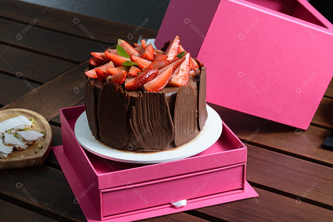 Bolo de chocolate sendo decorado coberto com morangos, folhas frescas de manjericão