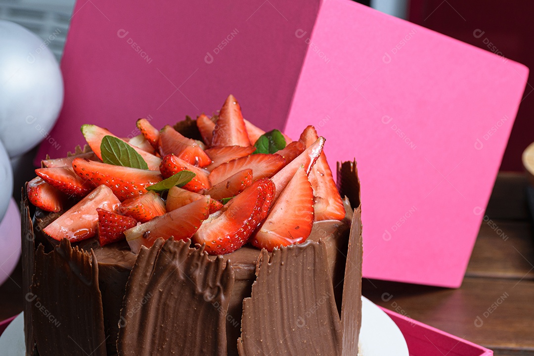 Bolo de chocolate sendo decorado coberto com morangos, folhas frescas de manjericão