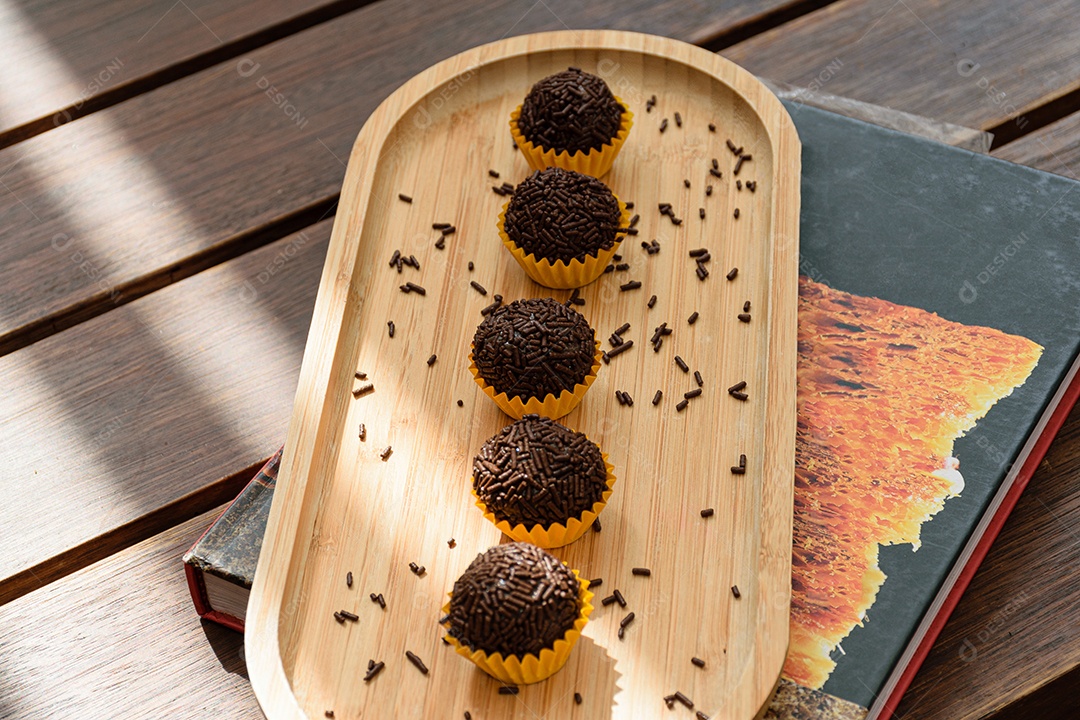 Brigadeiro enfileirado, iluminado e com pirulitos de chocolate ao fundo.