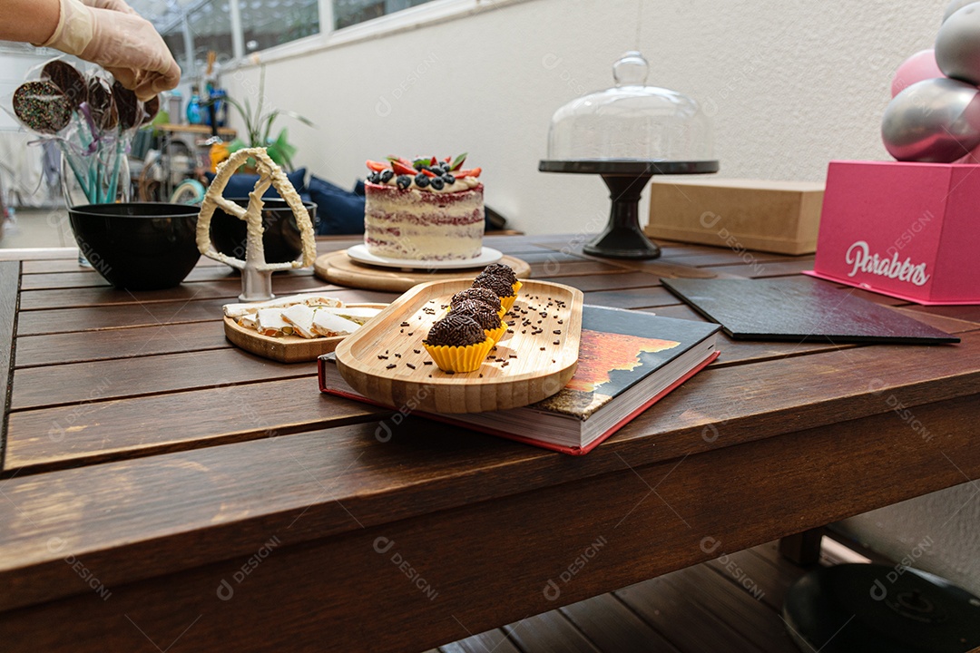 Brigadeiro enfileirado, iluminado e com pirulitos de chocolate ao fundo.