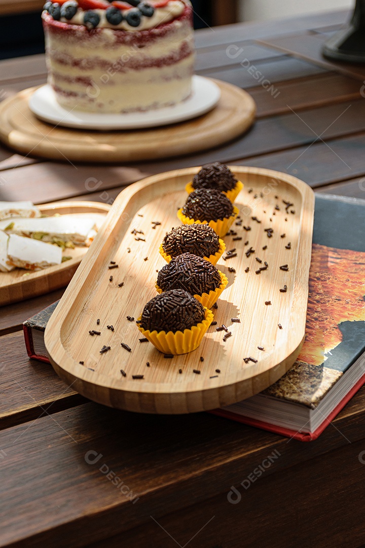 Brigadeiro enfileirado, iluminado e com pirulitos de chocolate ao fundo.