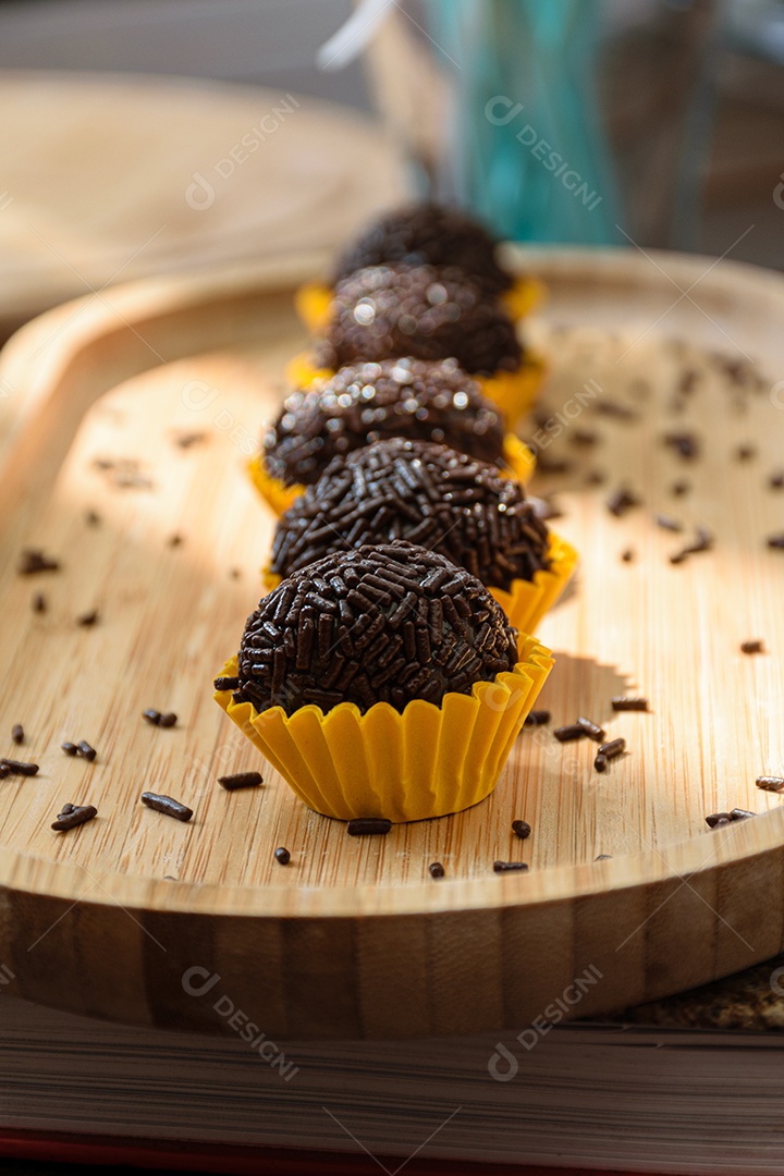 Brigadeiro enfileirado, iluminado e com pirulitos de chocolate ao fundo.