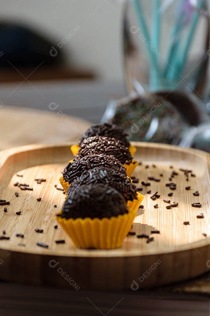 Brigadeiro enfileirado, iluminado e com pirulitos de chocolate ao fundo.
