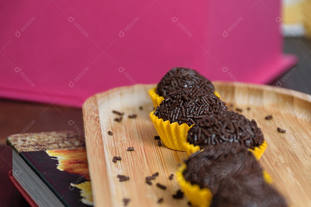 Brigadeiros alinhados em uma placa de madeira. O foco é o brigadeiro no centro.