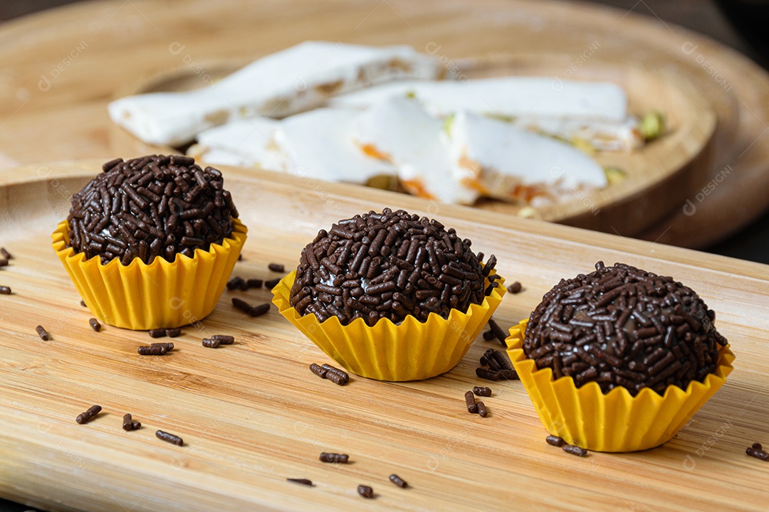 Brigadeiros alinhados em uma placa de madeira. O foco é o brigadeiro no centro.