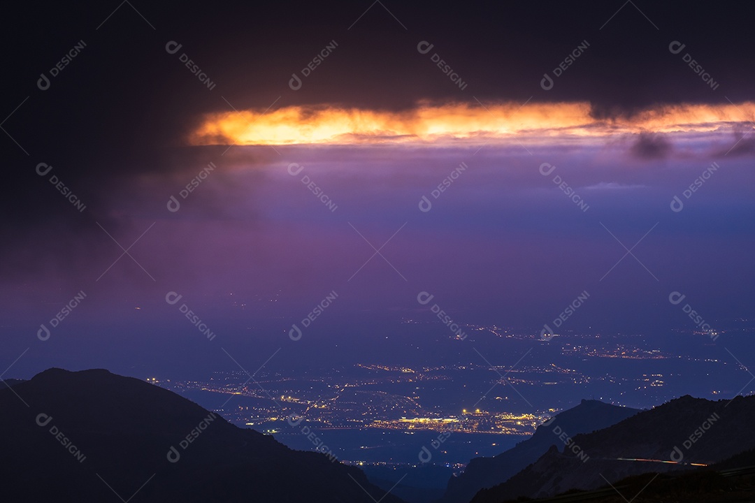 Vista da Serra Nevada com pequena estrada e cidade de Granada ao pôr do sol.