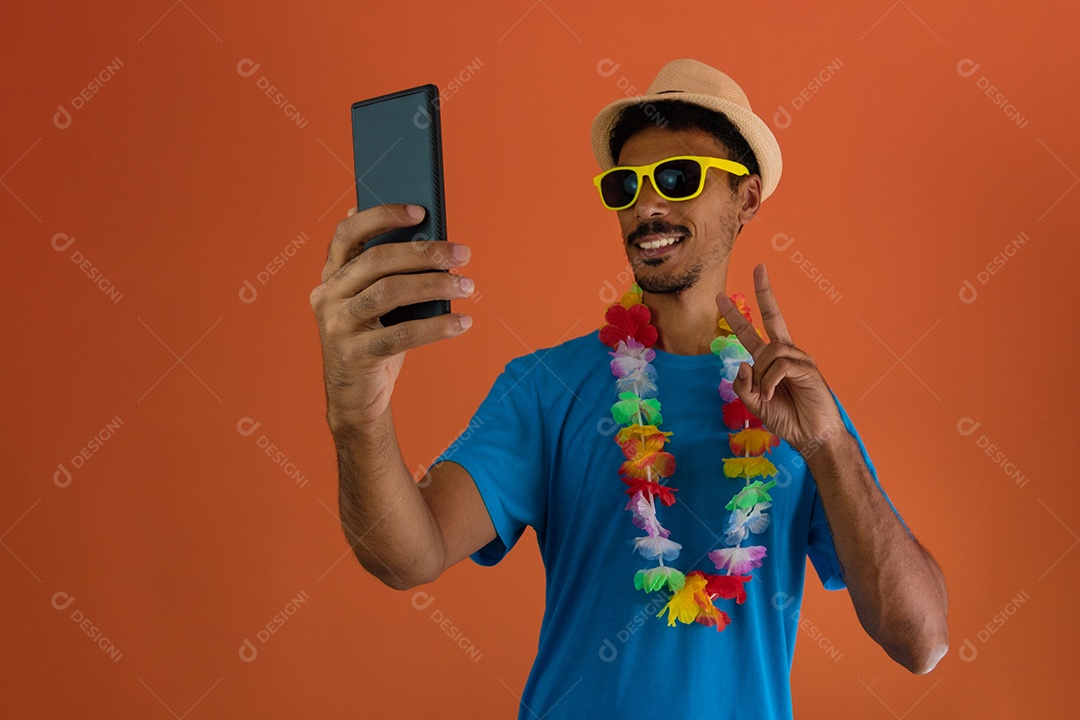 Homem negro fantasiado para o carnaval do brasil segurando o celular isolado em fundo laranja.
