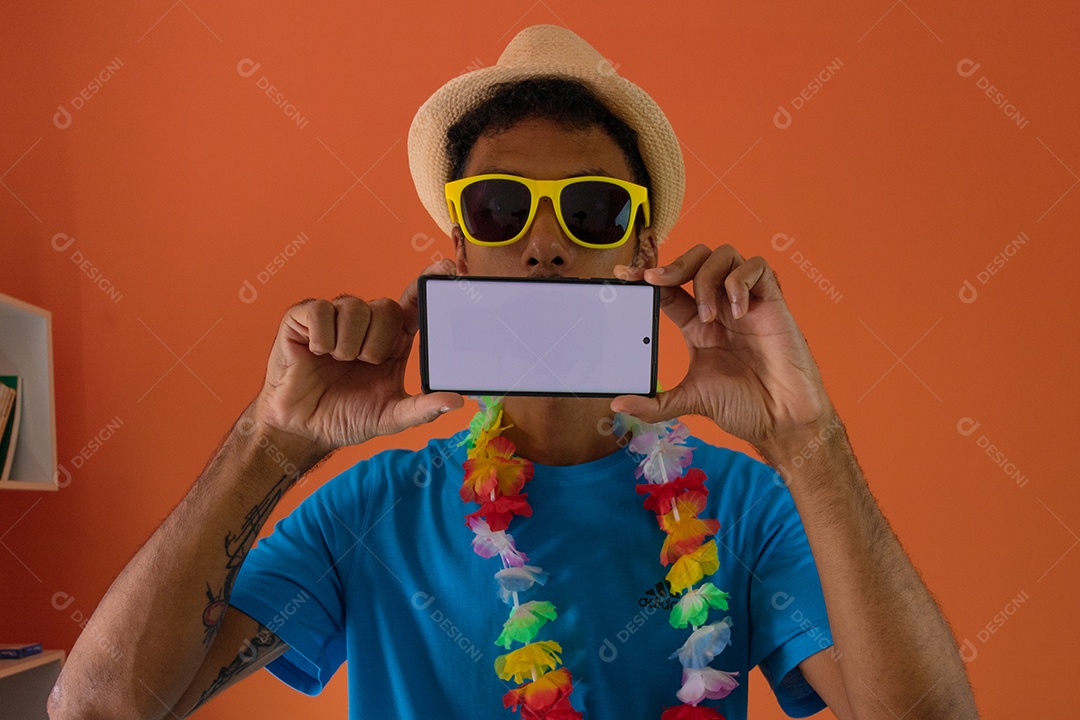 Homem negro fantasiado para o carnaval do brasil segurando o celular isolado em fundo laranja.