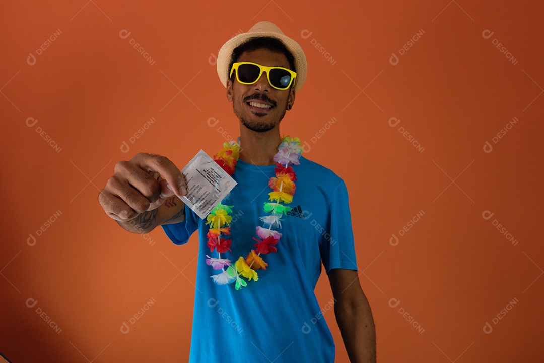 Homem negro fantasiado para o carnaval do brasil segurando um preservativo isolado em fundo laranja.