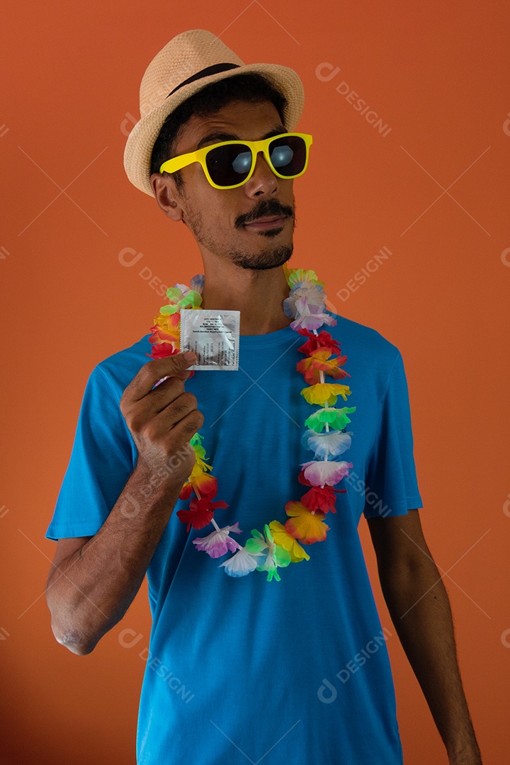 Homem negro fantasiado para o carnaval do brasil segurando um preservativo isolado em fundo laranja.