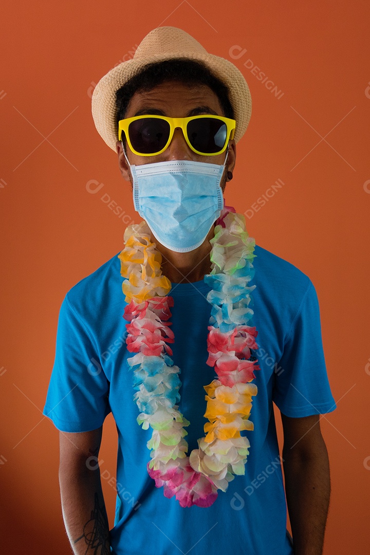 Homem negro em fantasia de carnaval e máscara pandêmica segurando um celular isolado em fundo laranja.