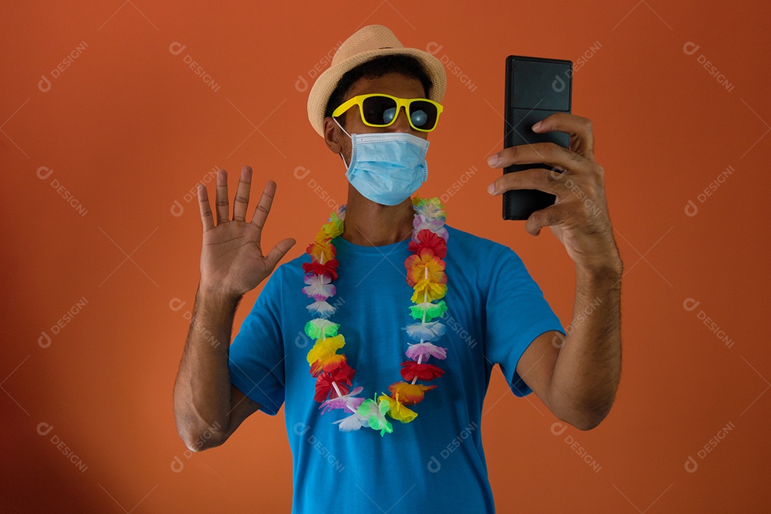 Homem negro fantasiado para o carnaval do brasil segurando o celular isolado em fundo laranja.