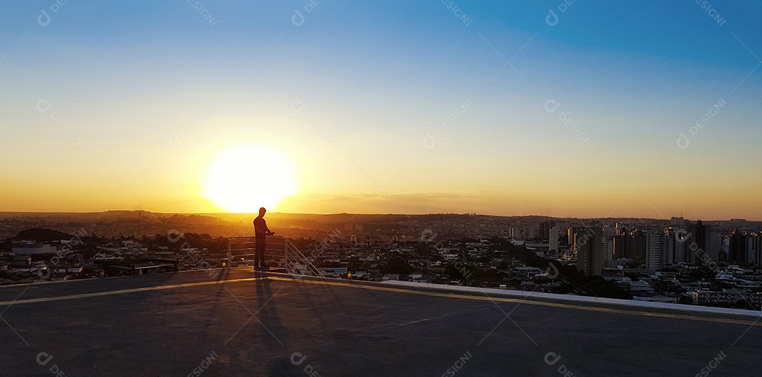 Silhueta de um homem no topo de um edifício por do sol na cidade
