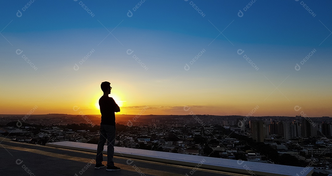 Silhueta de um homem no topo de um edifício por do sol