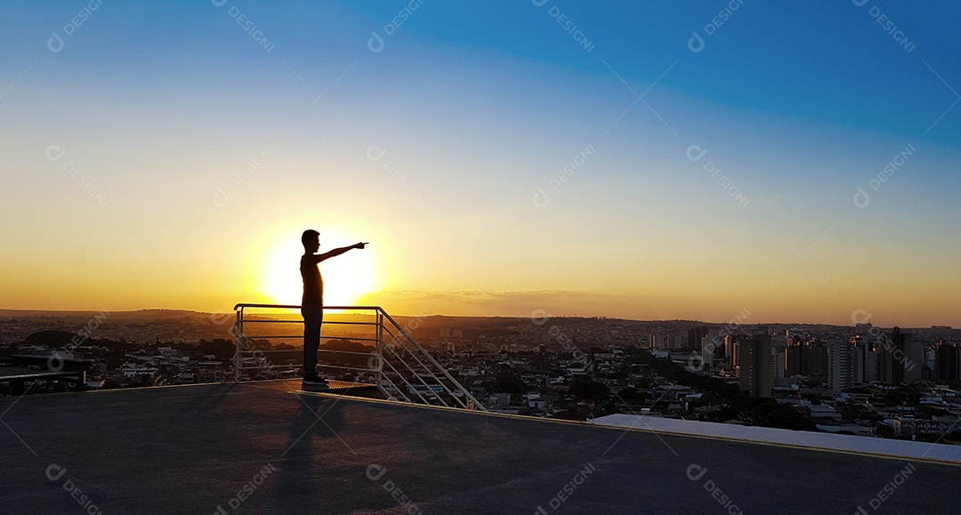 Silhueta de um homem no topo de um edifício por do sol na cidade