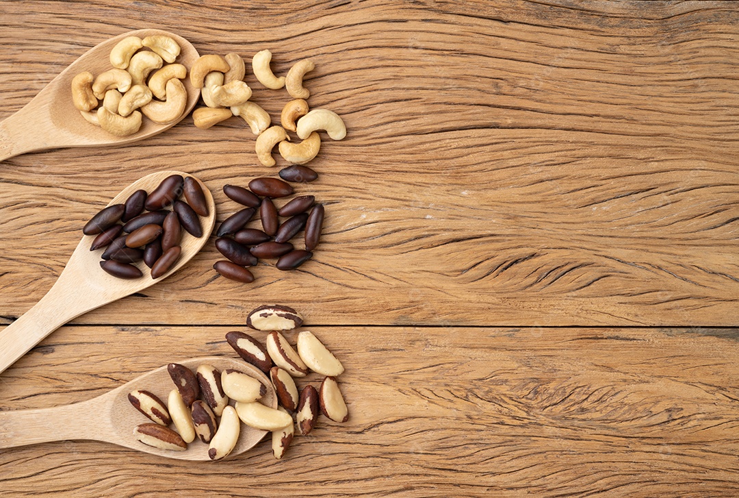 Castanha do Pará em colheres sobre mesa de madeira. Brasil, baru e castanha de caju