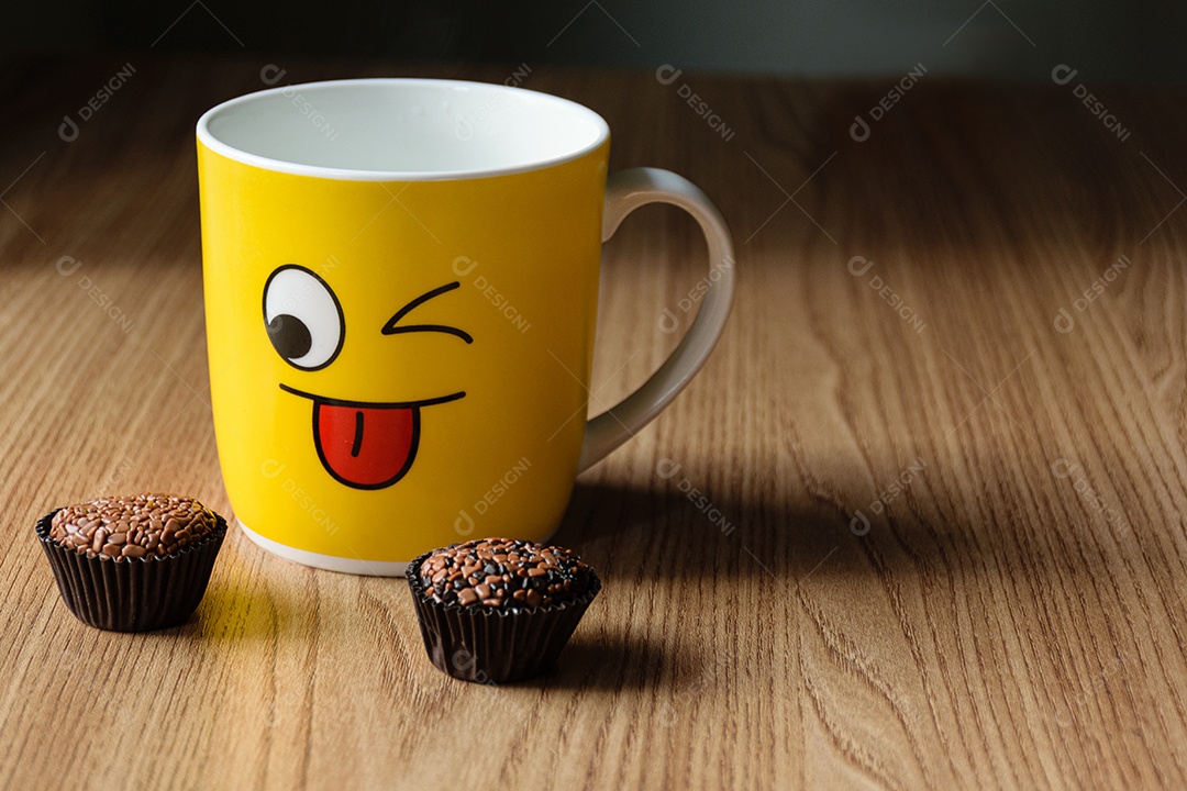 Caneca amarela com um caderno ao fundo, com dois brigadeiros desfocados