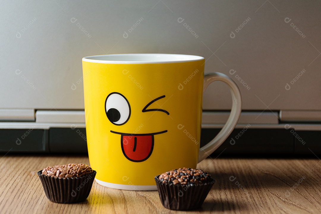 Caneca amarela com um caderno ao fundo, com dois brigadeiros desfocados