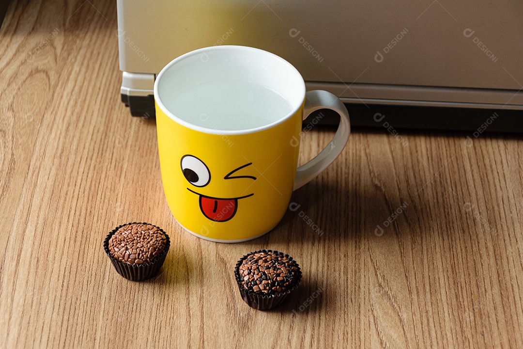 Caneca amarela com um caderno ao fundo, com dois brigadeiros desfocados