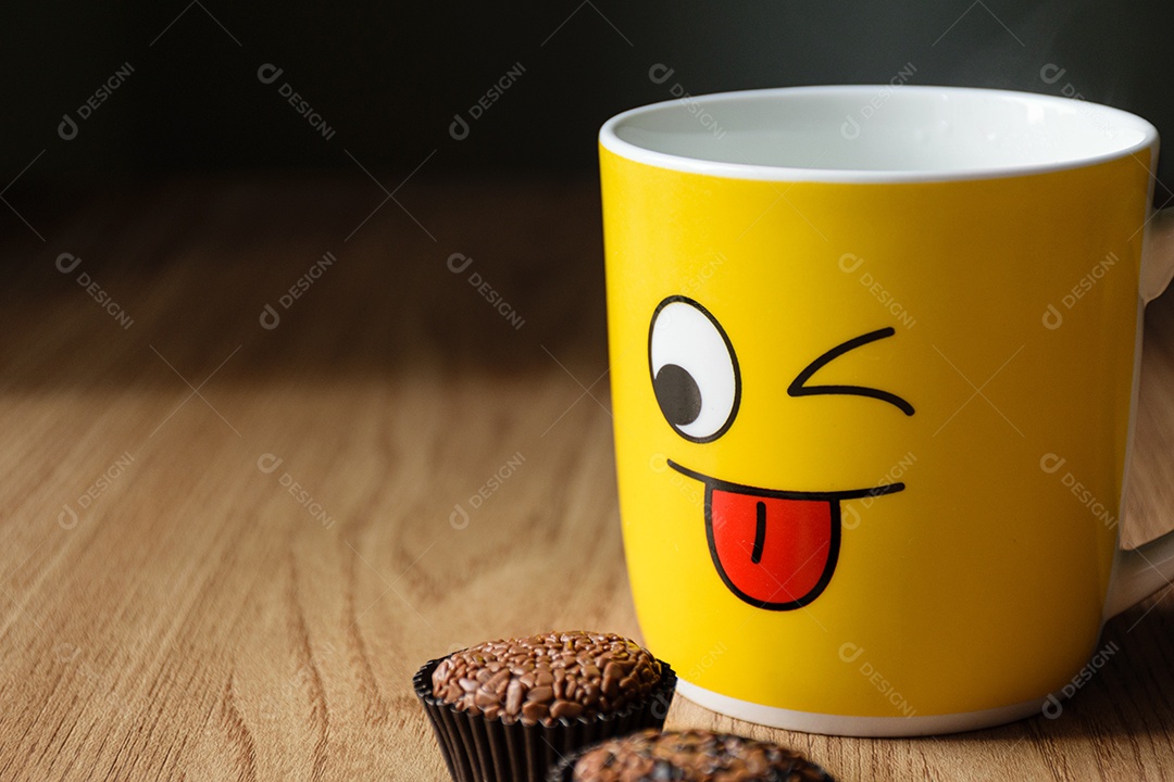 Caneca amarela com um caderno ao fundo, com dois brigadeiros desfocados