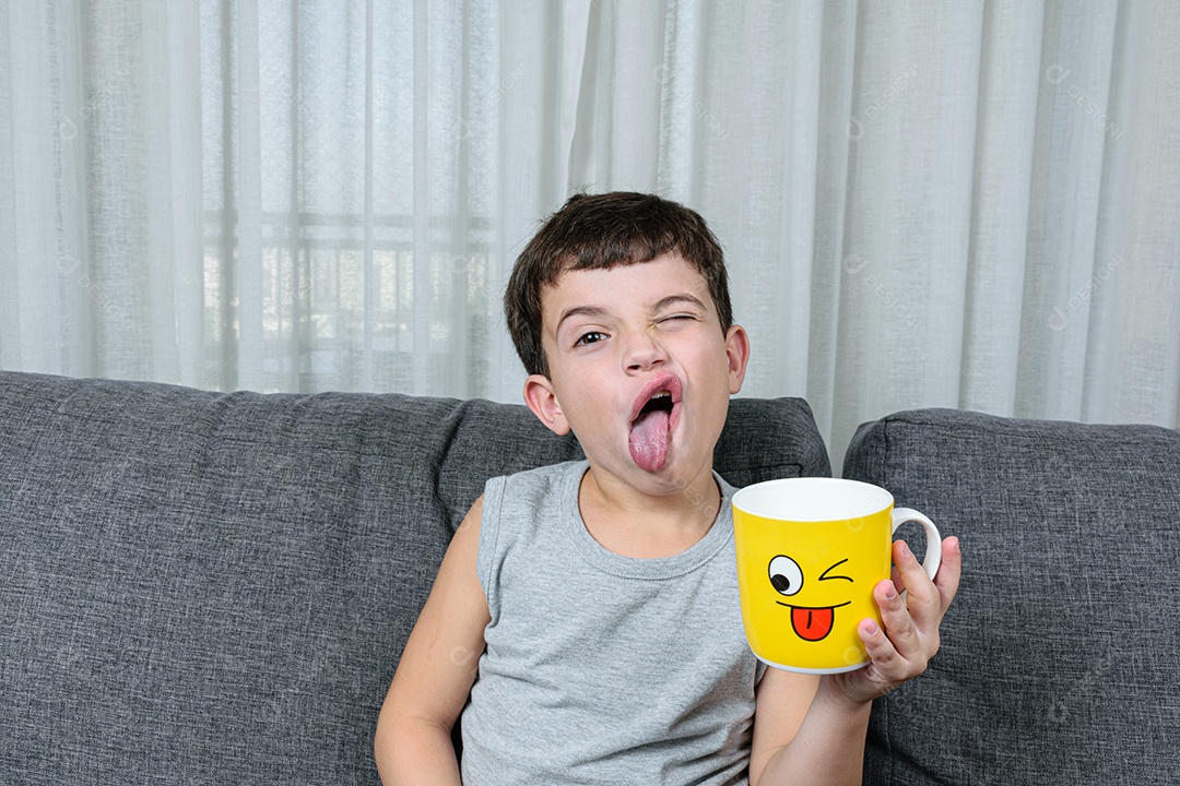 Criança de 7 anos fazendo careta e segurando uma caneca amarela.
