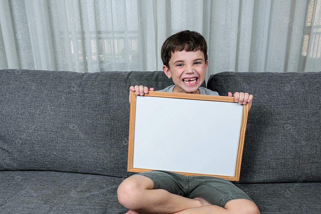 Criança de 7 anos sentada no sofá e segurando um quadro branco.