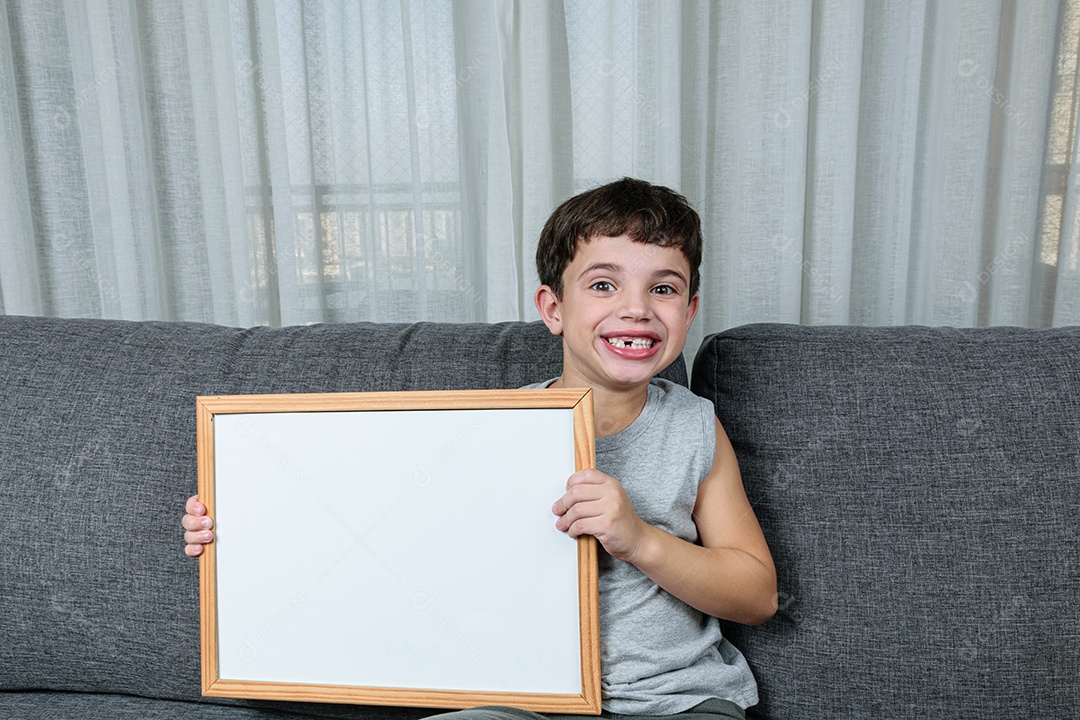 Criança de 7 anos sentada no sofá e segurando um quadro branco.