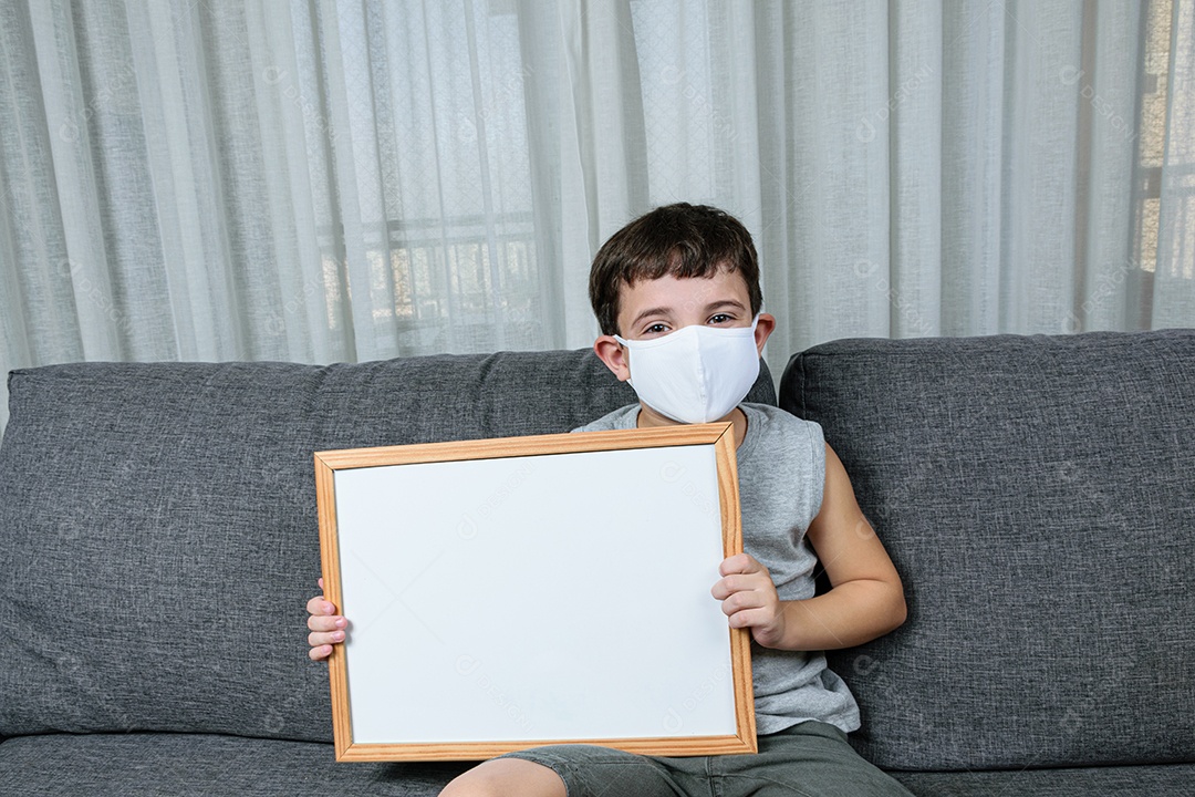 Criança de 7 anos sentada no sofá e segurando um quadro branco.