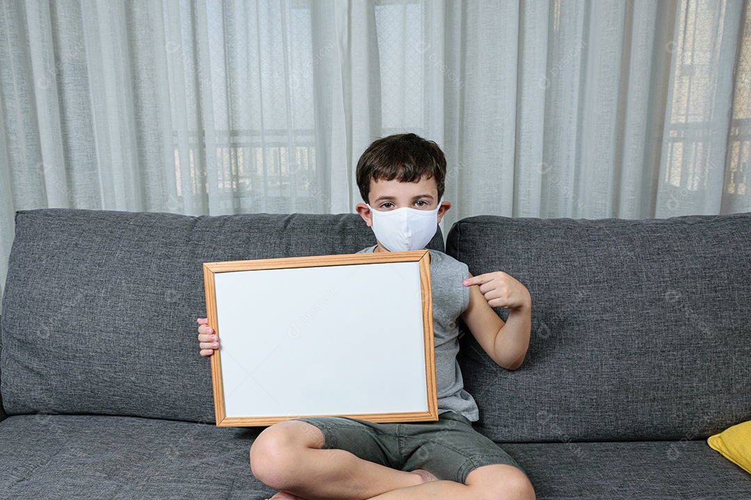 Criança de 7 anos sentada no sofá e segurando um quadro branco.