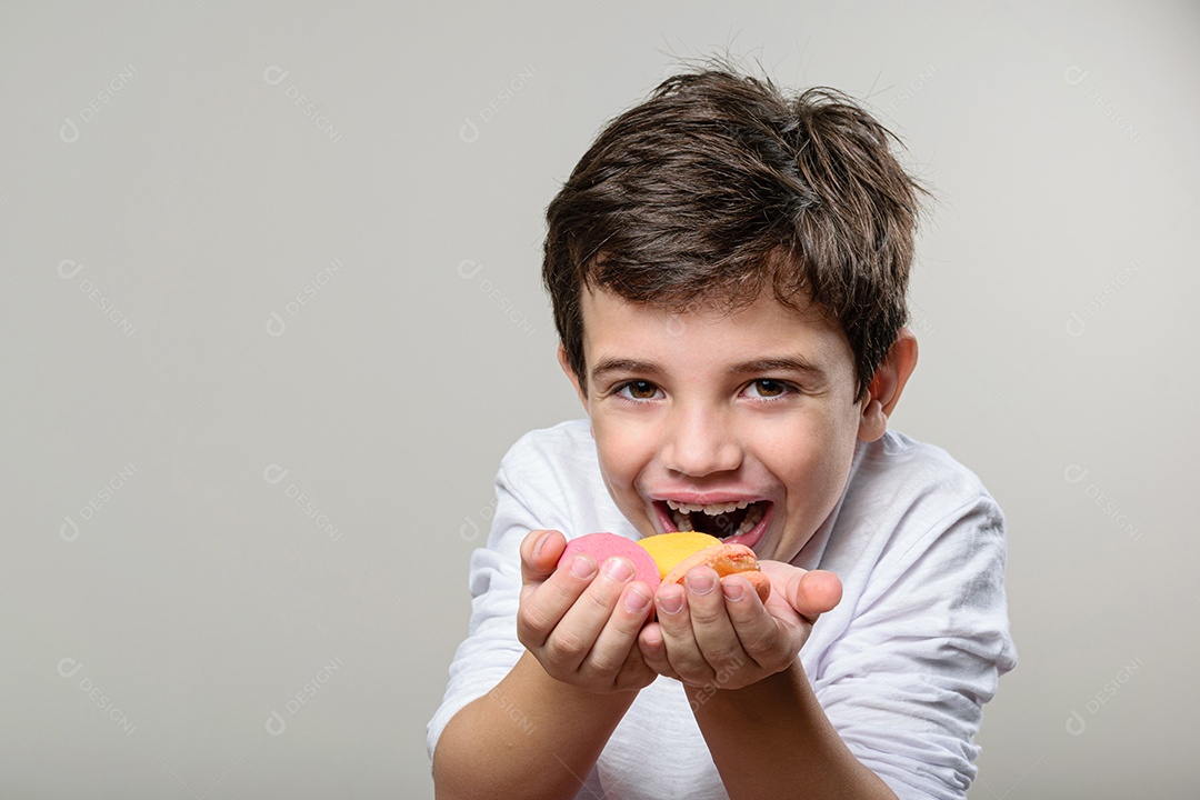 Criança de 6 anos segurando um biscoito rosa e com um grande sorriso no rosto.