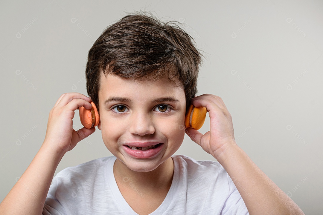 Criança de 6 anos segurando um biscoito rosa e com um grande sorriso no rosto.
