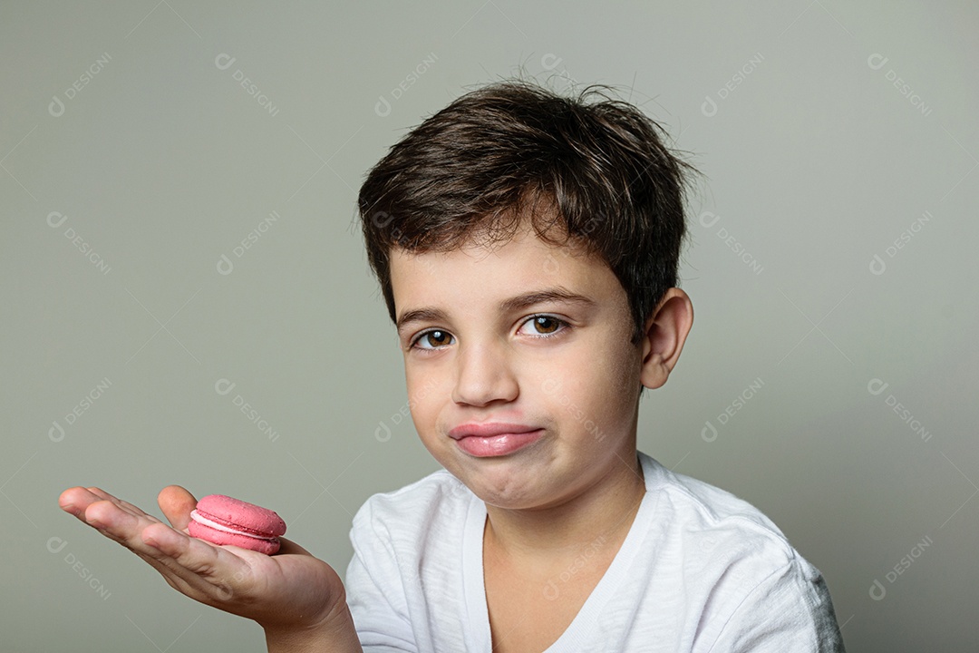 Criança de 6 anos segurando um biscoito rosa e com um grande sorriso no rosto.