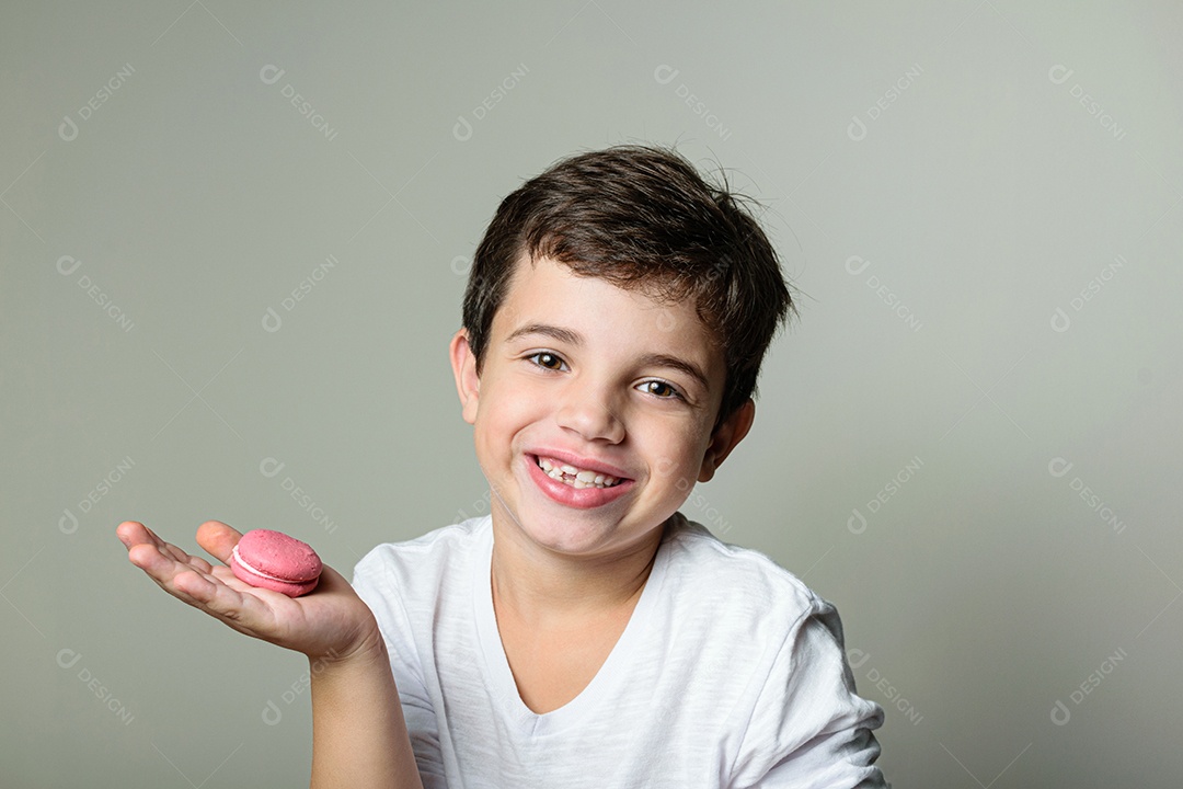 Criança de 6 anos segurando um biscoito rosa e com um grande sorriso no rosto.