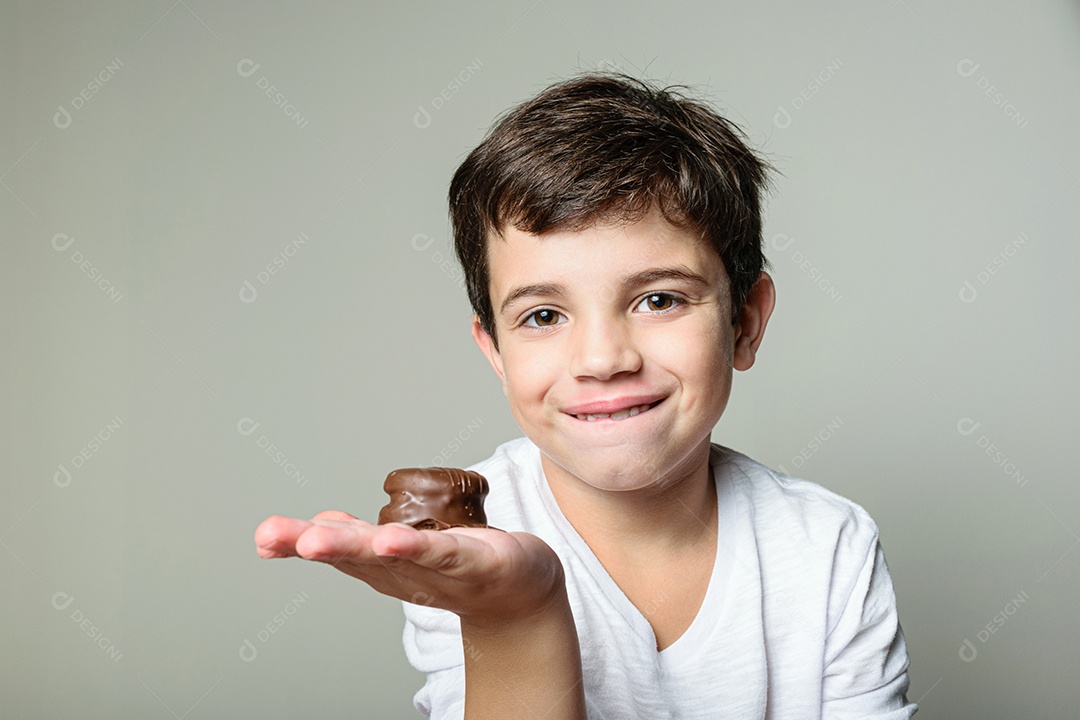 Criança de 6 anos segurando um biscoito rosa e com um grande sorriso no rosto.